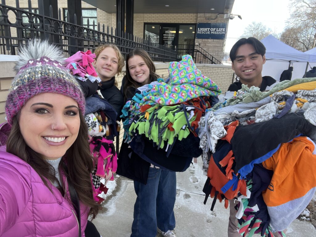 Students hold arm fulls of blankets outside Light of Life rescue mission