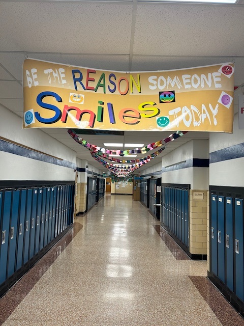 A banner emblazoned with "be the reason somebody smiles" hangs in the hallway as a paperchain can be seen zig zagging down the ceiling