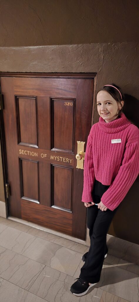 student stands by a door that says Department of Mysteries