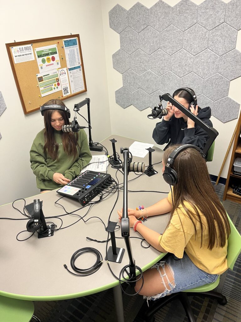 students speak into a microphone with headphones over their ears